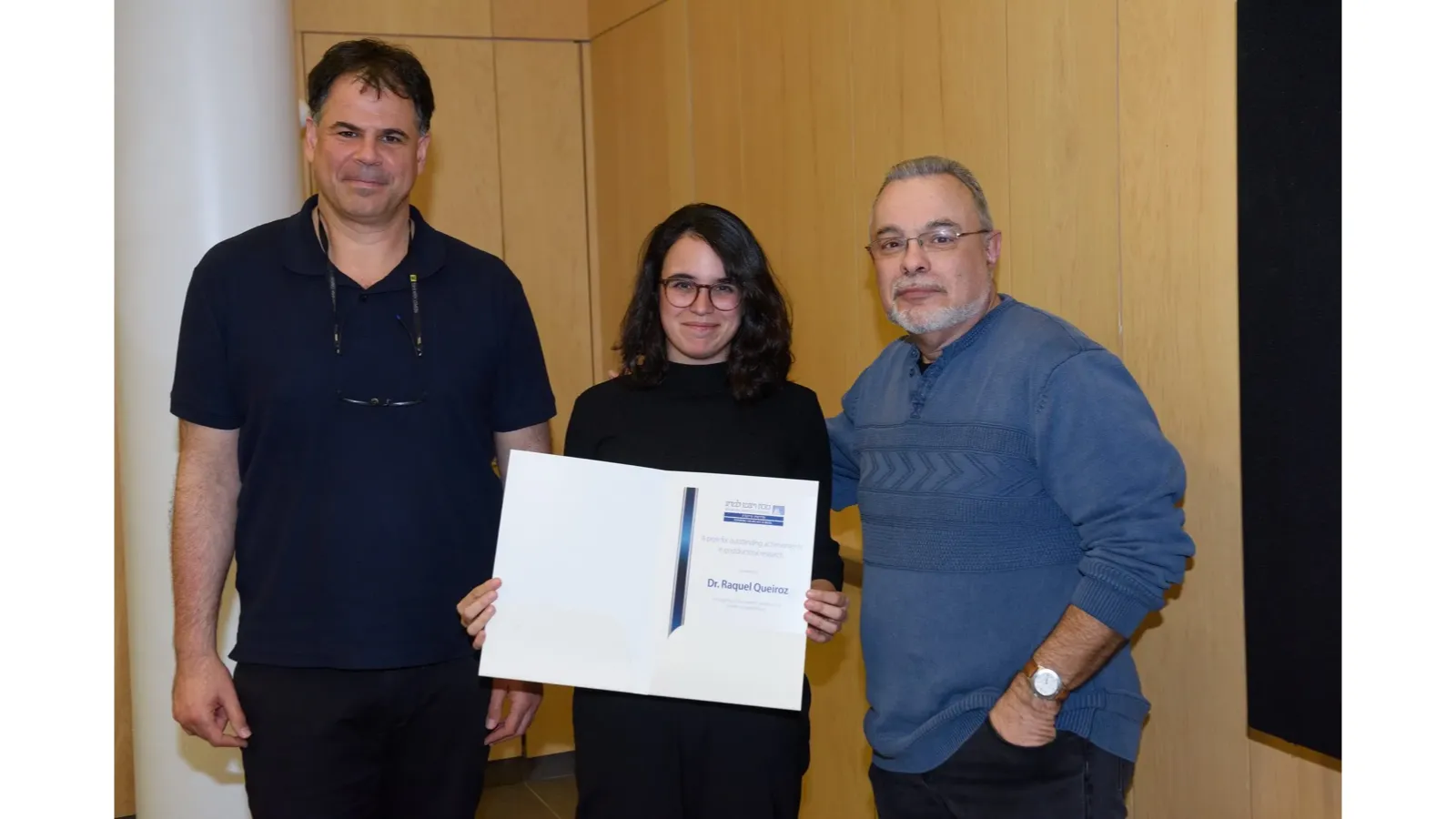 Raquel Queiroz holding her postdoctoral research prize certificate with two presenters